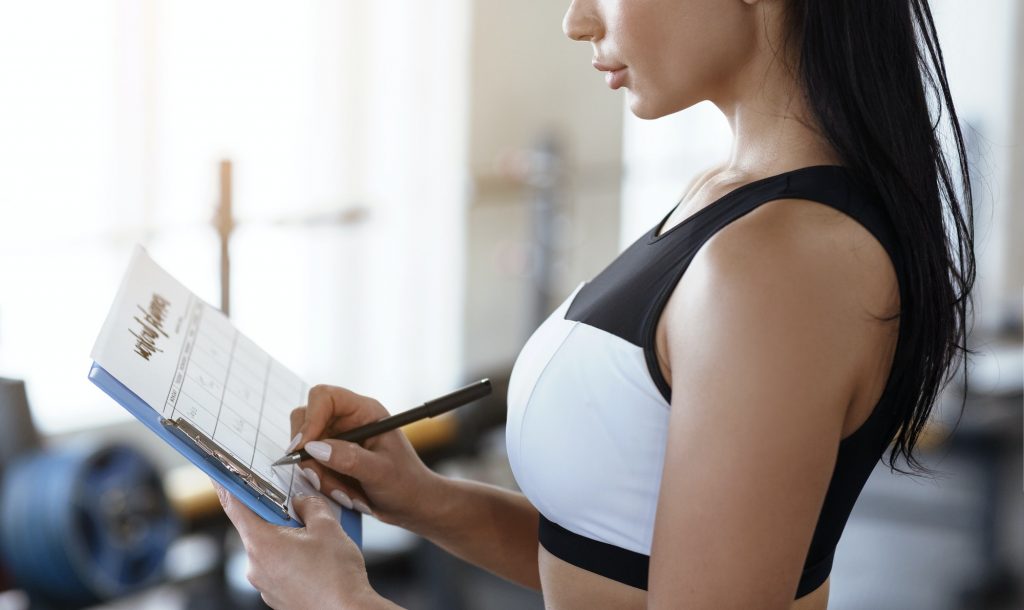 Workout planning. Young woman keeping track of her trainings in gym, closeup