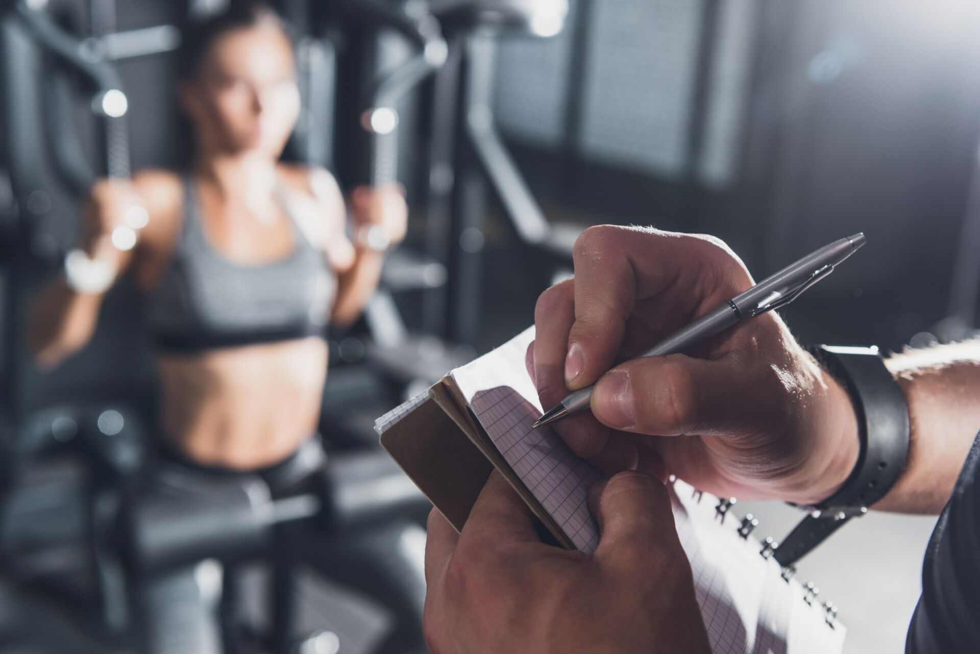 close up view of trainer writing in notebook while woman working out in gym