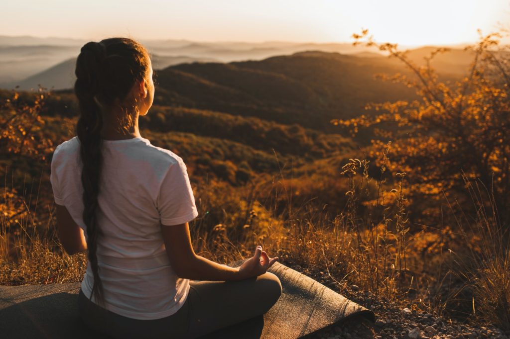 Woman meditating alone on hill with amazing autumn mountain view at sunset. Zen spiritual