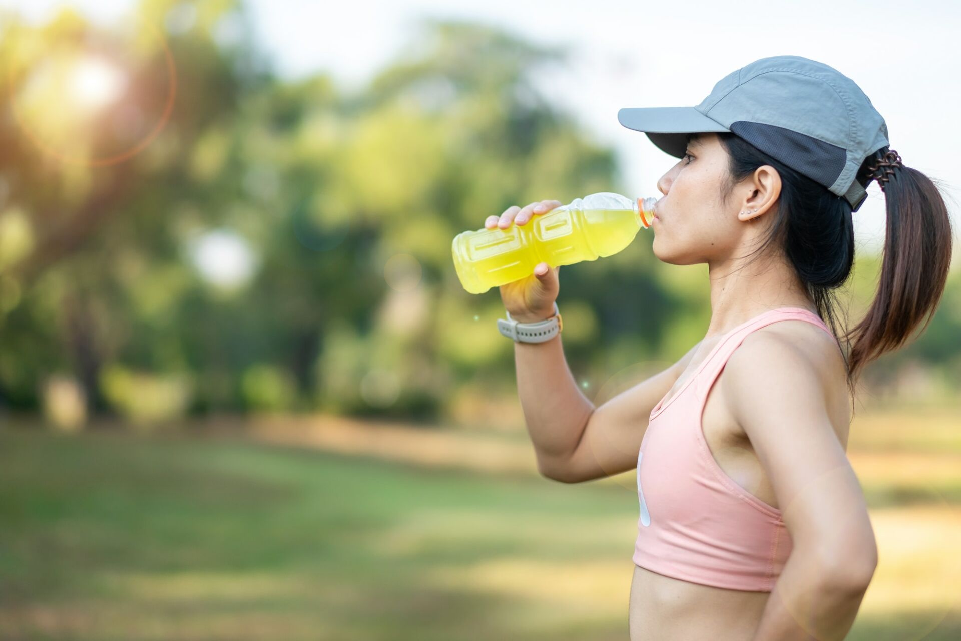 young fitness woman drinking energy water during stretching muscle in the park outdoor