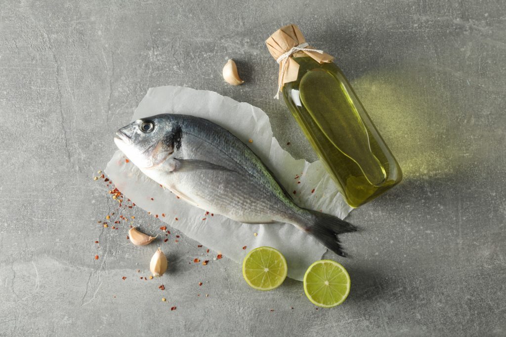 Dorado fish, oil and spices on grey background, top view