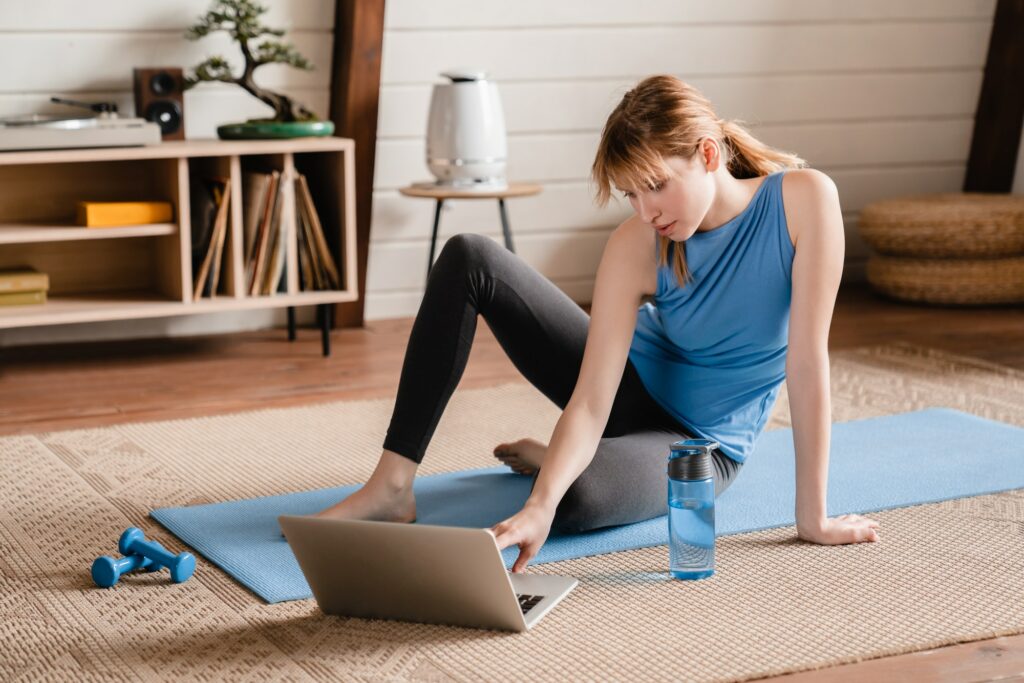 Young female athlete using laptop on exercise mat for sport fitness tutorial